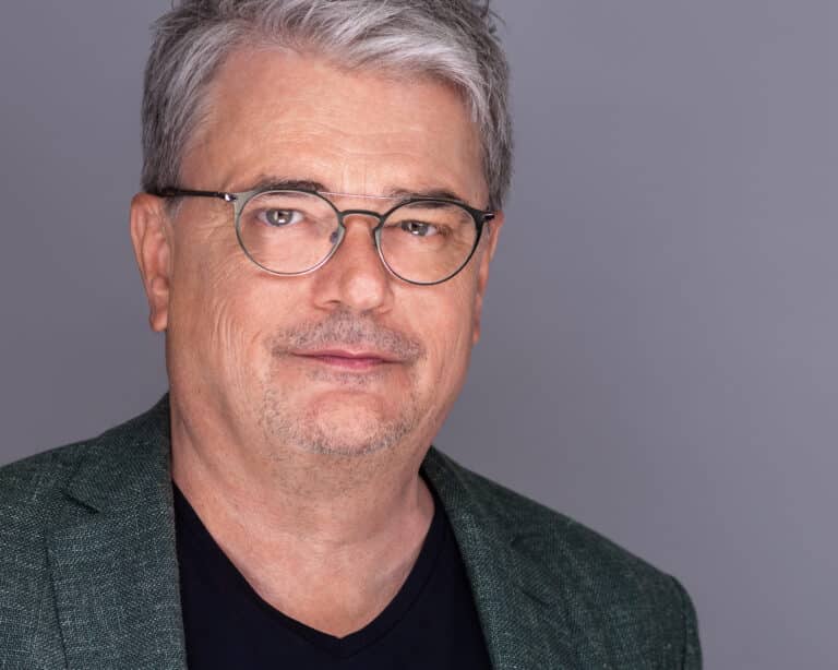 männliche Person, grünes Sakko, Brille, graues Haar, Lächeln